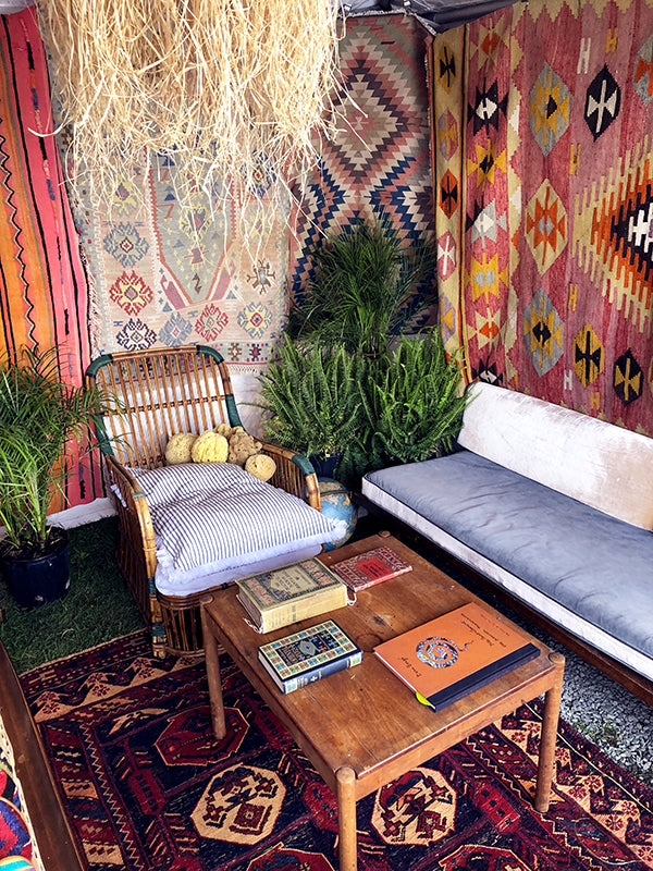 antique carpet books displayed on table on kilim carpet surrounded by whicker furniture and kilim rugs.