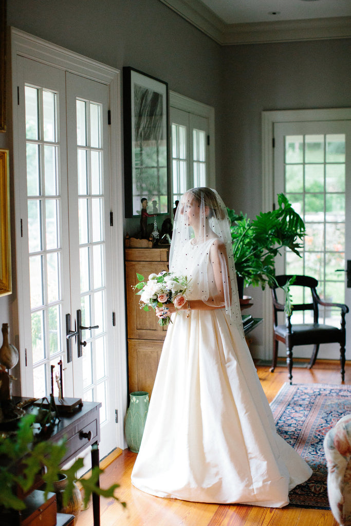 bride wearing her wedding dress and pearl velvet slippers looking out the window holding her bouquet.