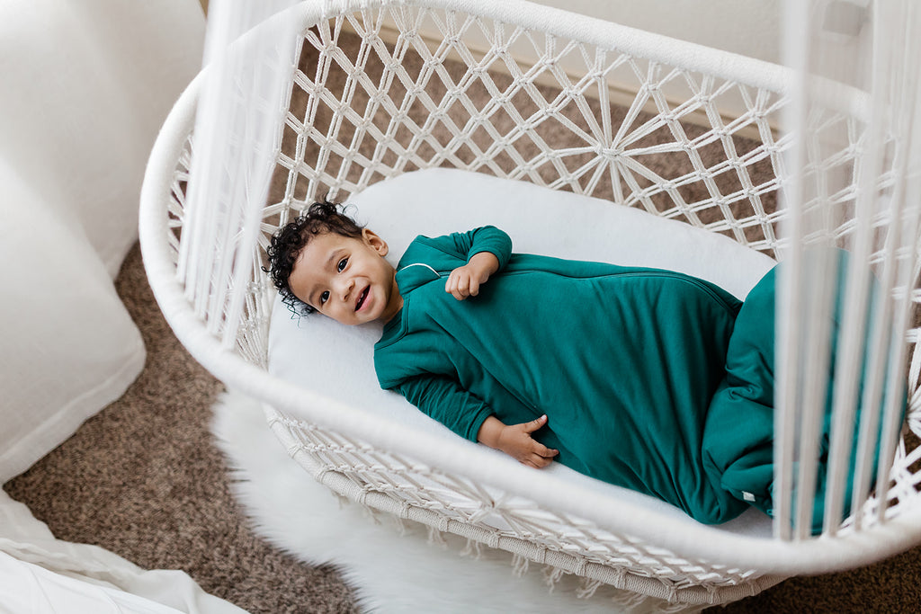 happy baby in an emerald green bamboo sleep sack and macrame bassinet