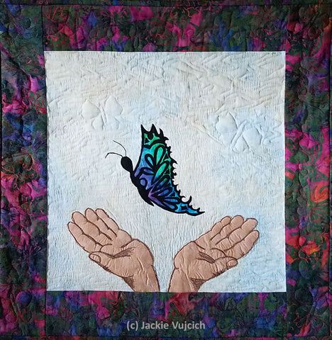 If you love them set them free pictorial art quilt  by Jackie Vujcich depicting to hands letting a butterfly fly free. Featured in a blog post by Jackie Vujcich of Colorado Creations Quilting