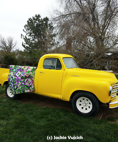 1950 yellow Ford truck with a quilt hung over the side.  Savvy Strips quilt pattern by Jackie Vujcich is available at Colorado Creations Quilting
