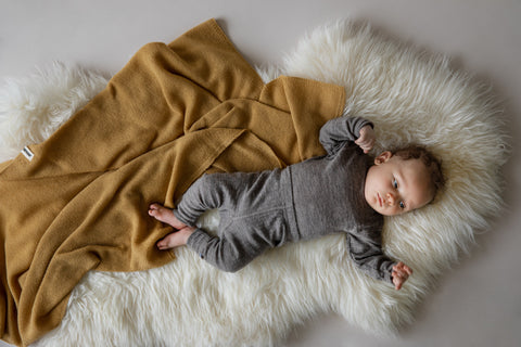 A baby lying on a lambswool with a merino wool blanket