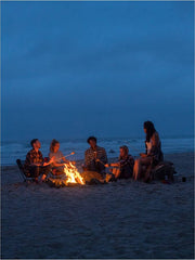 Group of campers around a campfire roasting marshmallows and wearing Flyshacker flannel shirts