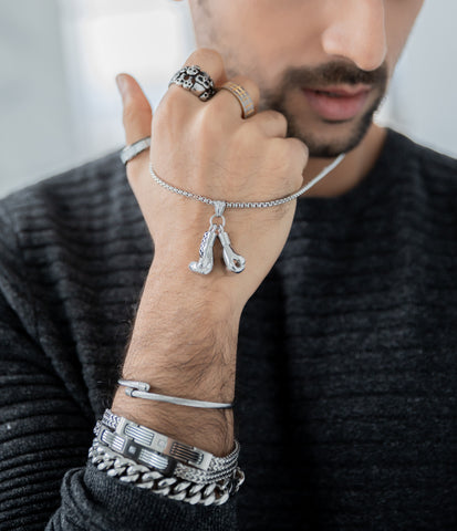 Indian male model wearing grey sweater while modeling an assortment of silver stainless steel jewelry including a silver boxing glove pendant necklace 