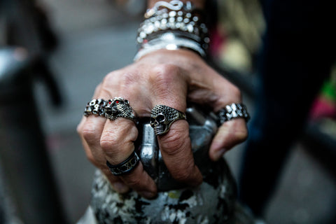 Caucasian model wearing silver skull head and lion head silver 316L high- grade stainless steel rings holding a fountain stand outside in chinatown manhattan rings handmade and designed by playhardlookdope 