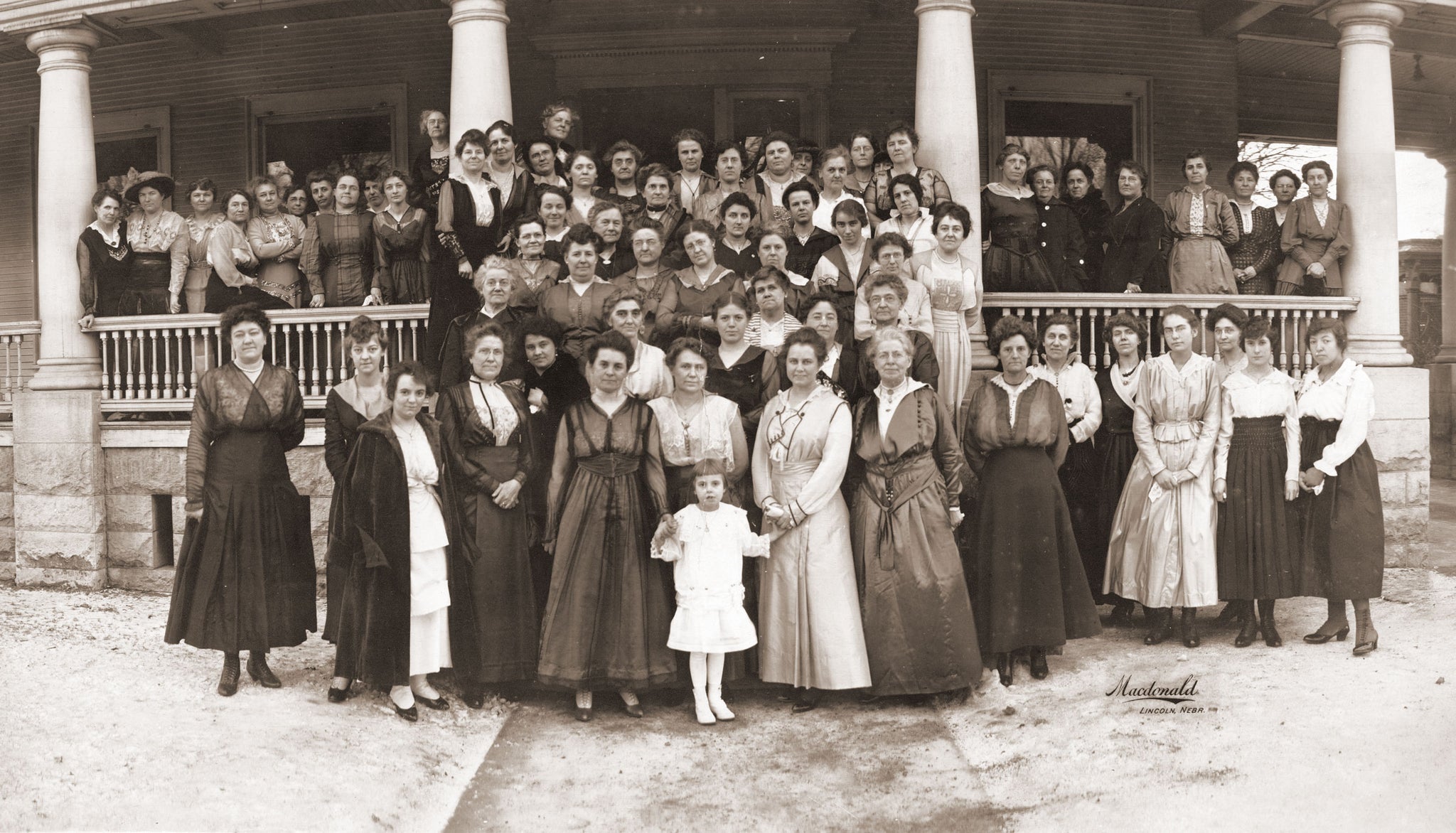 Nebraska Legislative Ladies League in front of the Governor's mansion, Lincoln, 1917. Gov. Keith Neville was Governor from 1917 to 1919. In this photo, Mrs. Neville was taking over as honorary president from Mrs. Morehead. The little girl in front is Mary Nelson Neville. -- Courtesy Nebraska State Historical Society