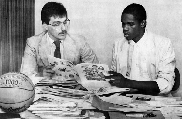 MASH head basketball coach Norm Price helping standout player Mike Burnett review the stacks of college recruiting materials that came in for him, 1987. Price coached the team for 23 years over two stints before retiring in 2013. Price had 413 wins while at the helm of the Bulldogs, leading them to a state runner-up finish in 1986-1987. -- Courtesy of Norm Price