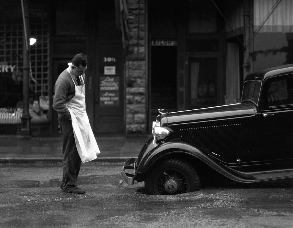 A car stuck in a pothole next to Cut Rate Grocery, 1936. -- Mason City Public Library Archives