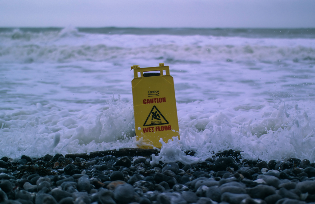 Caution wet floor (house or office cleaning sign) placed by waves from the sea