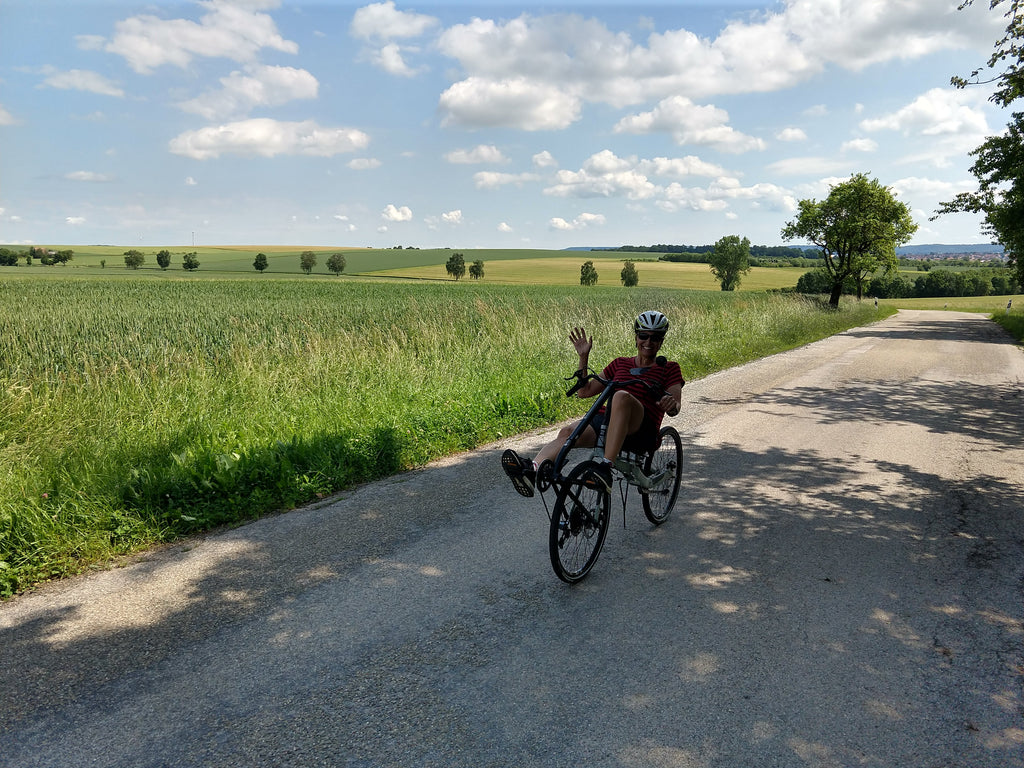 Photo of Maria waving from her Cruzbike Q45 adventure touring recumbent bike in the Bavarian countryside