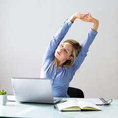 A woman working from home and stretching in front of her laptop