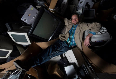 Drew laying in a pile of discarded computers and televisions looking cool and relaxed wearing the circuit board tie. A visual representation of being the King of E-Waste.