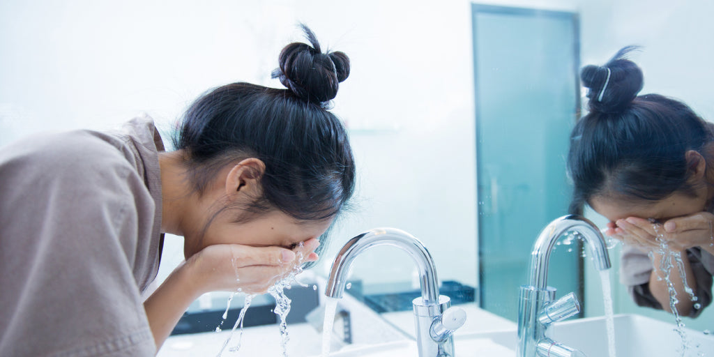 young woman washing her face with water at sink