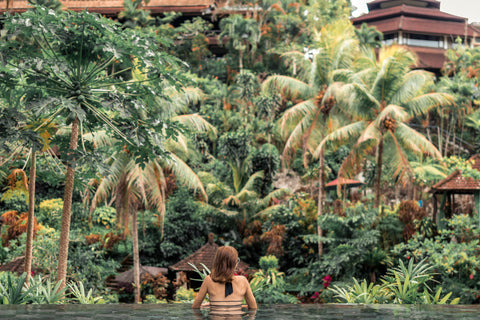 Woman in an infinity pool in Bali, overlooking palm trees. Resorts in Bali are some of the best quality hotels in Indonesia. 