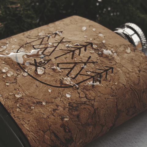 A Cork Wrapped Hip Flask engraved with a campsite image. Water droplets sit on the surface demonstrating its water resistant capabilities. Hip Flask by Hord.