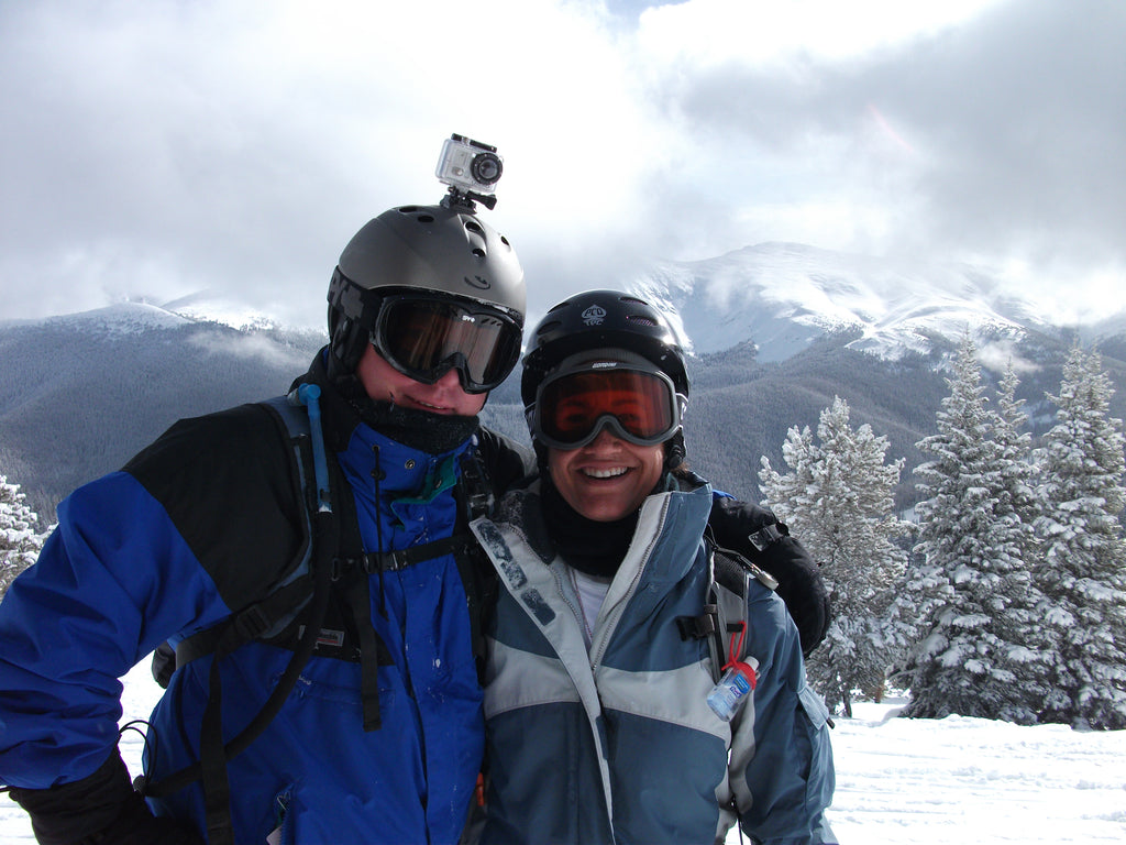 Founders, Lonnie and Melissa, wearing snowboard gear and winter apparel with snow covered mountains behind them.