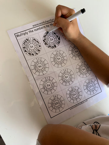 Child writing on laminated multiplication worksheet