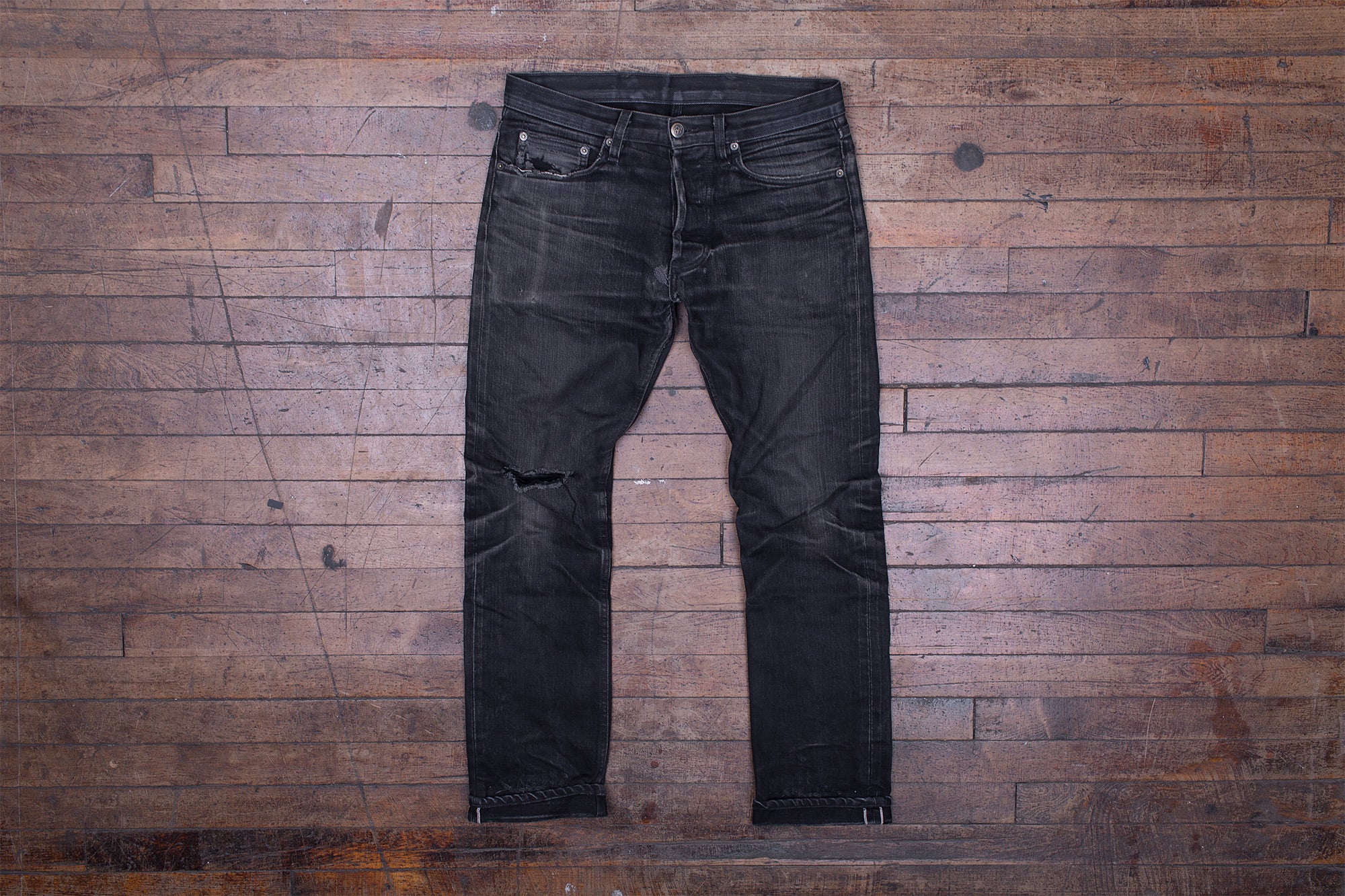 Front photo of a pair of worn-in black jeans laying on a wooden floor.