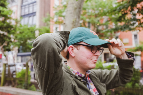 Chris adjusts and straightens his green ballcap with both hands.