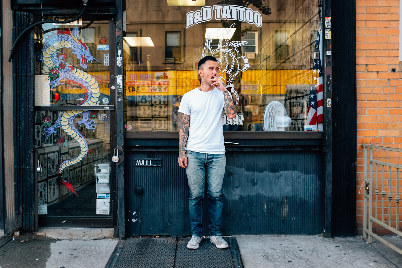 A man smokes a cigarette outside a tattoo shop.