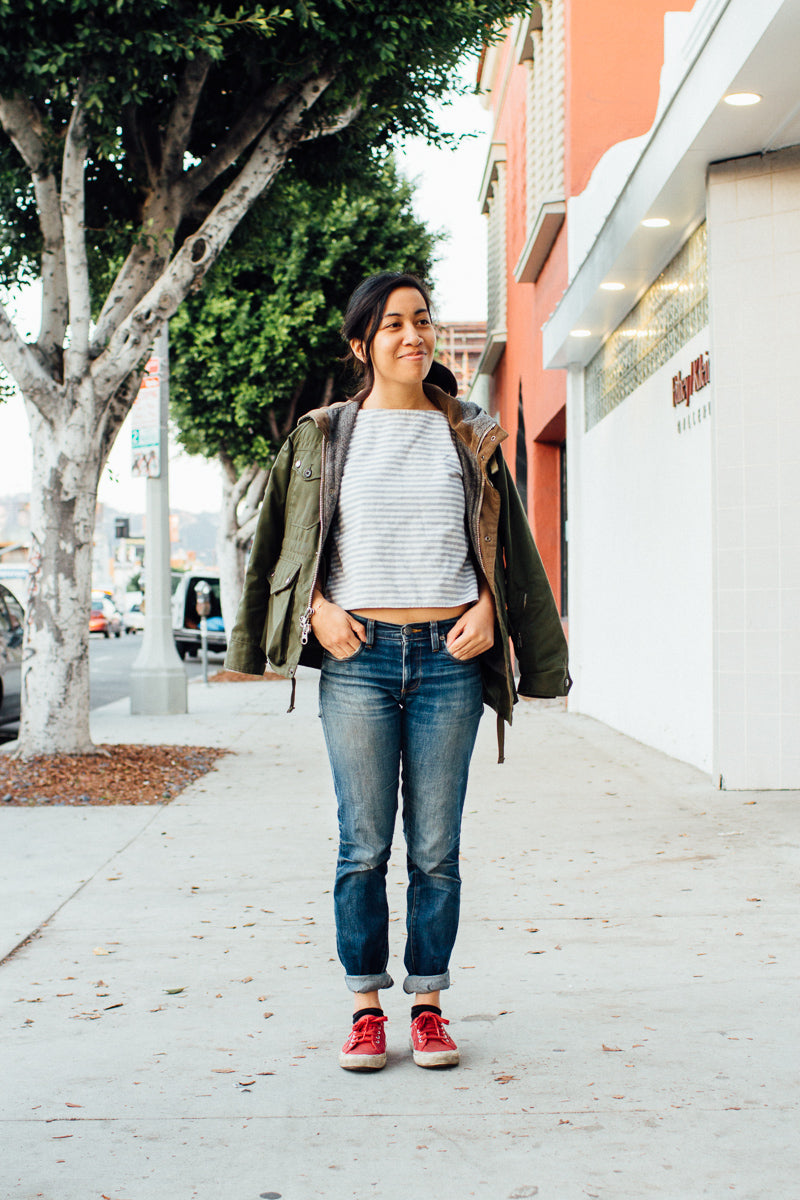 A young woman in faded blue jeans and an olive jacket.