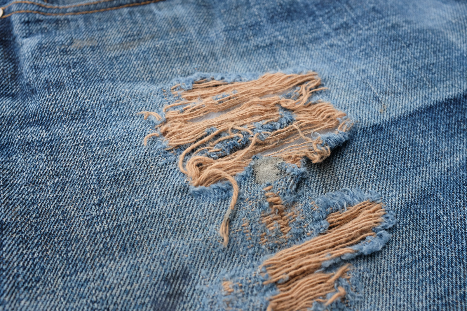 Detail shot of the front of the pair of jeans showcasing the brown weft fabric peeking through in areas that the indigo warp fabric has worn down.