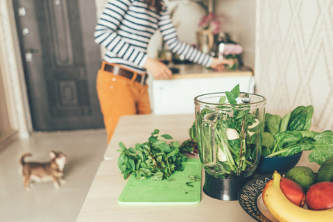 Woman prepares green smoothie with dog in background