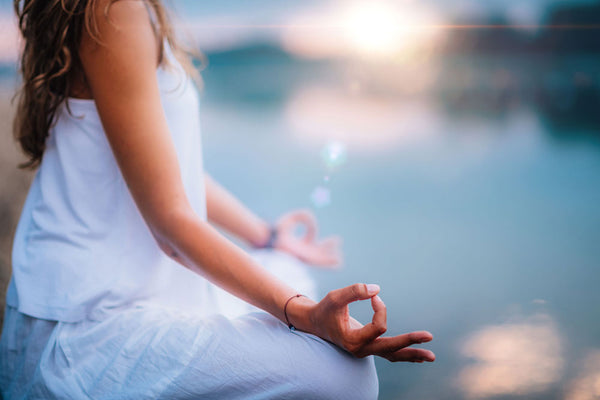 Image of a woman meditating by a lake at sunset to improve nutrient absorption