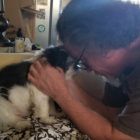 older man head to head embracing with small black and white special needs rescue dog
