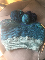Half-finished knitting with various small balls of teal yarn