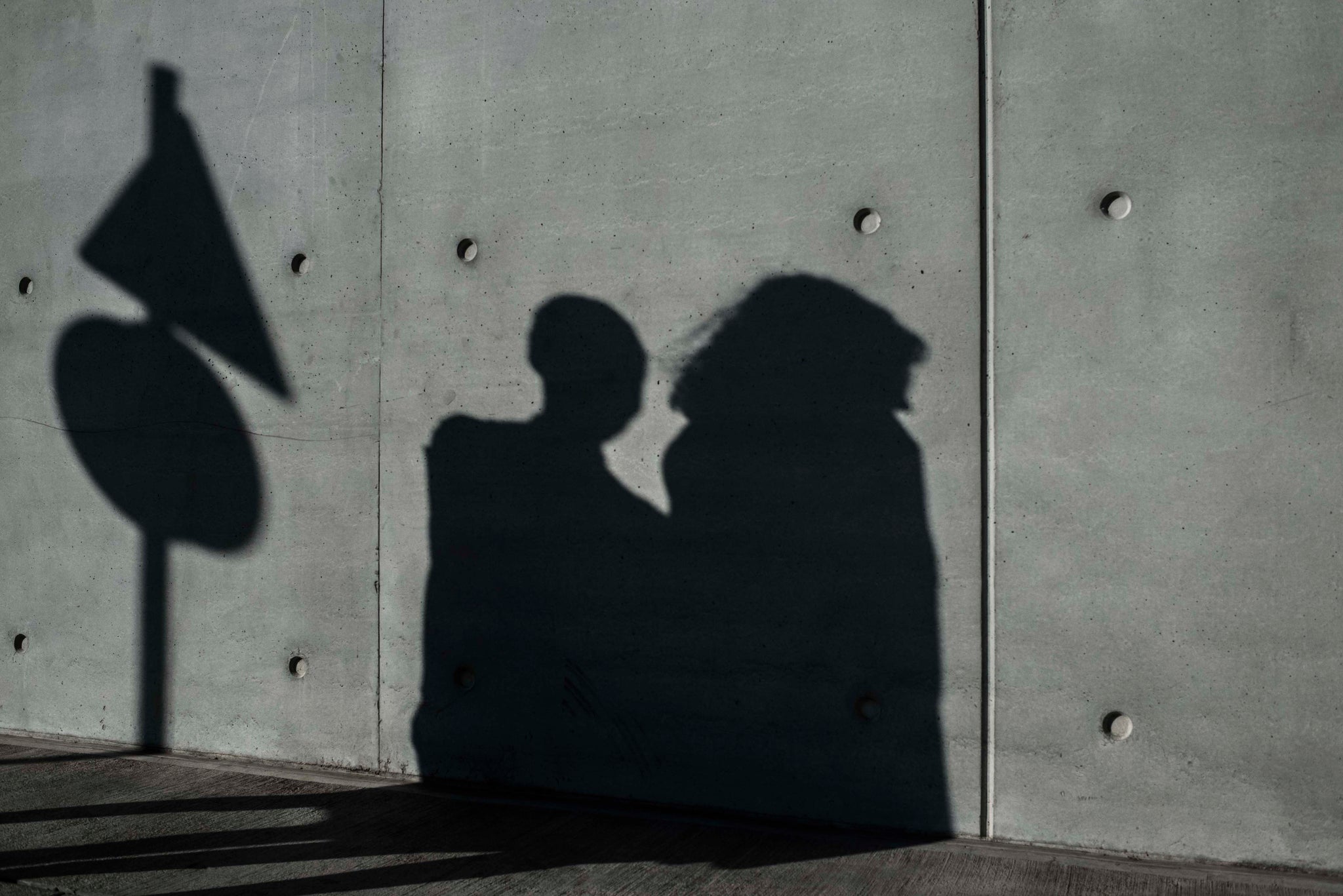 concrete wall with shadow of two women and sign post