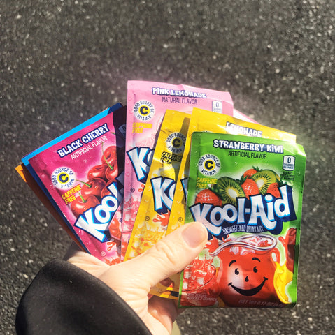 An image of a hand holding a variety of Kool-Aid packets. Part of a blog post by Amy Reader about how to dye yarn with Kool-Aid