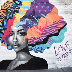 A black and while drawing of an african woman with massive colourful hair with lots of different designs.  Love is Colour is written on the wall beside her.  