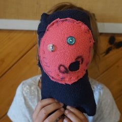 A child with a toy covering their face, obviolsy made by a child but a cute attempt at sewing for a first timer. 