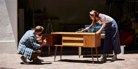 Two people refurbishing a wooden set of drawers