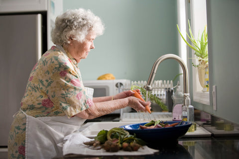 Elderly woman washing vegetables in a flowery dress