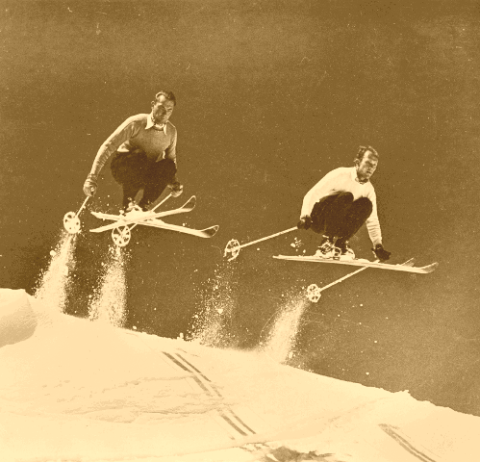 Two skiers catching air on vintage skis.