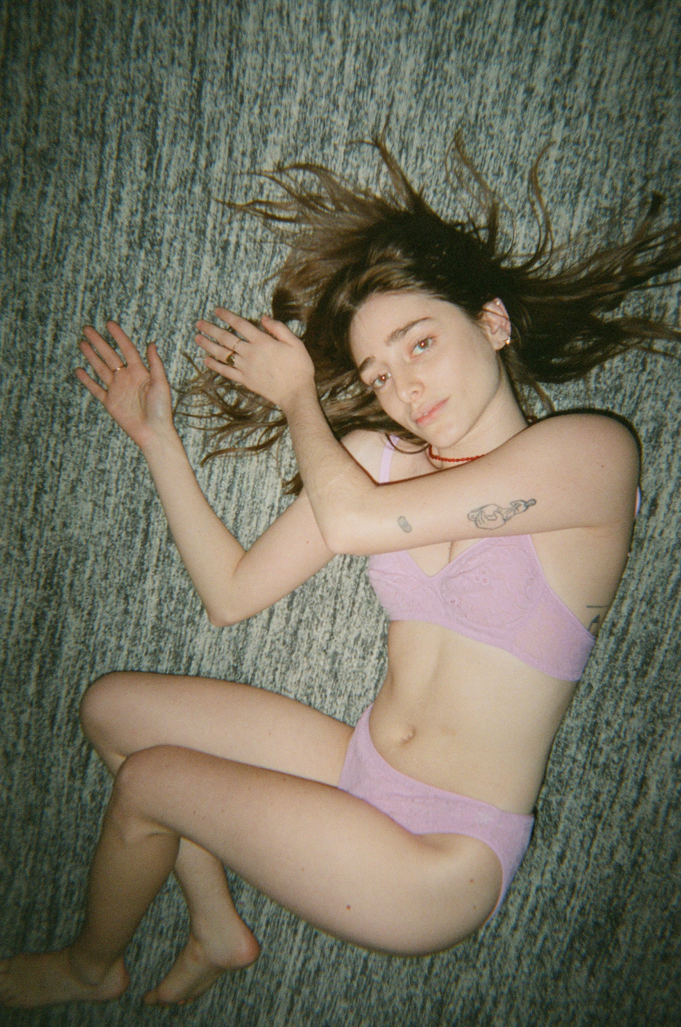 Woman in a pink bra and underwear laying on a carpet.