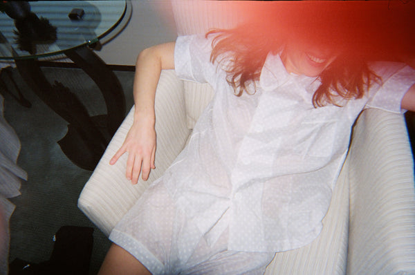 Woman in a white pajama shirt and shorts sitting on a chair with the camera flash blocking her face.