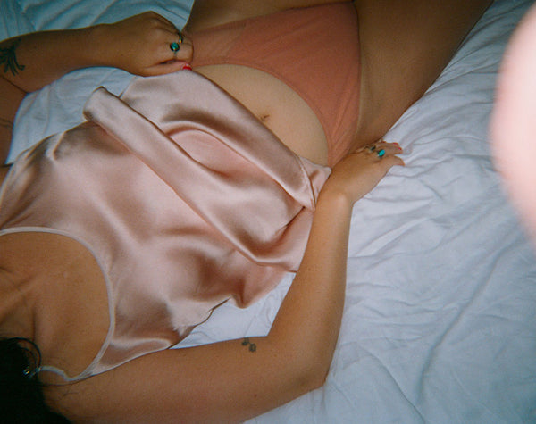 Woman laying on a bed in a pink chemise and beige tights.