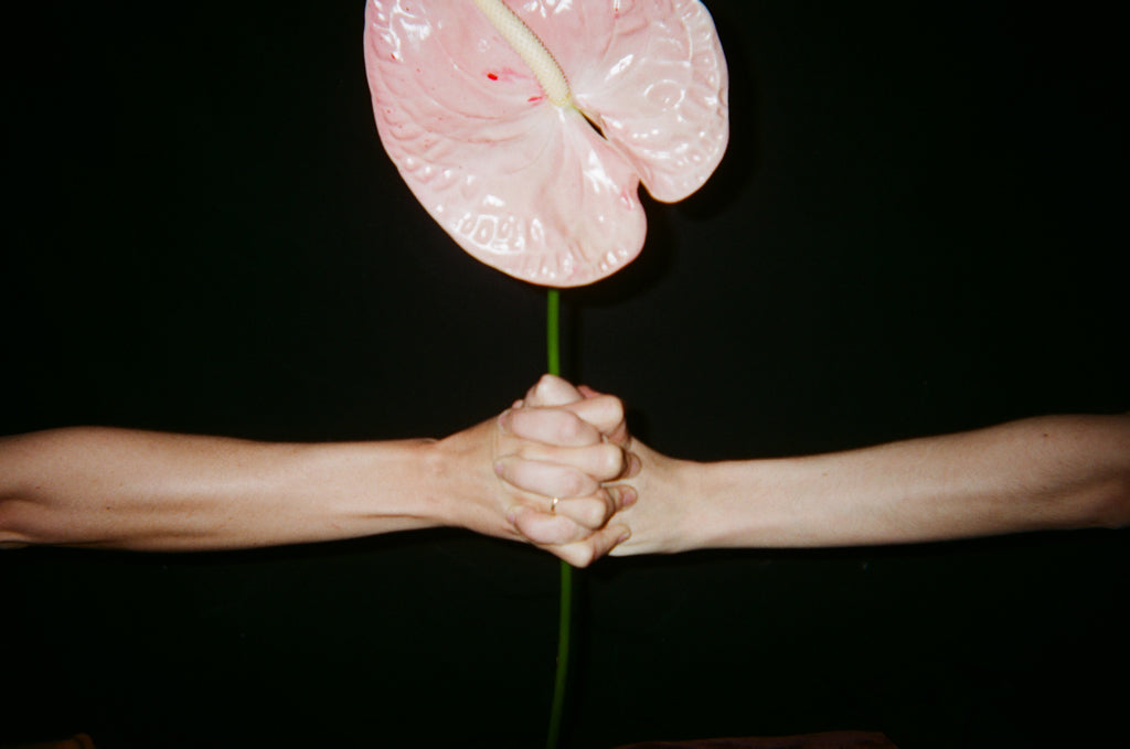 Two hands holding onto a stem with a glass pink flower.