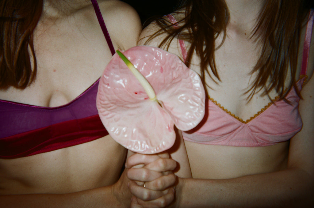 A woman in a purple bra and a woman in a pink bra holding onto a stem with a pink glass flower.
