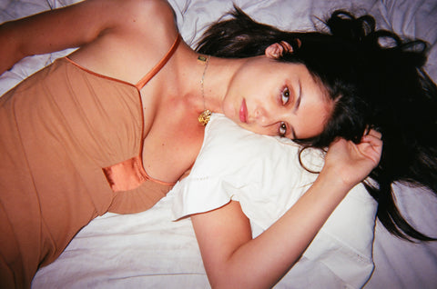 Woman in an orange tank laying on a bed.