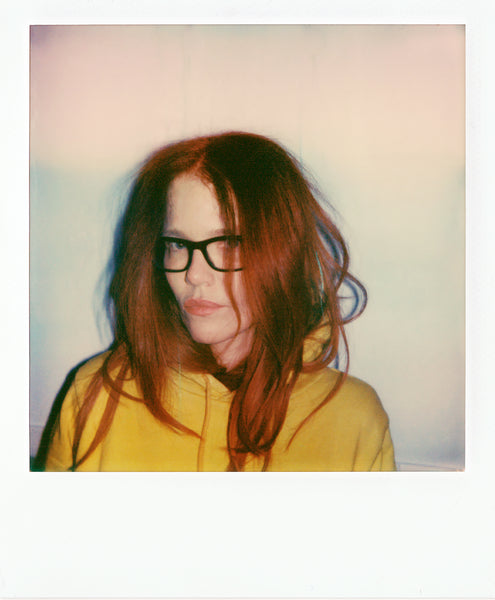 Up close view of a red haired woman with glasses in a yellow hoodie.
