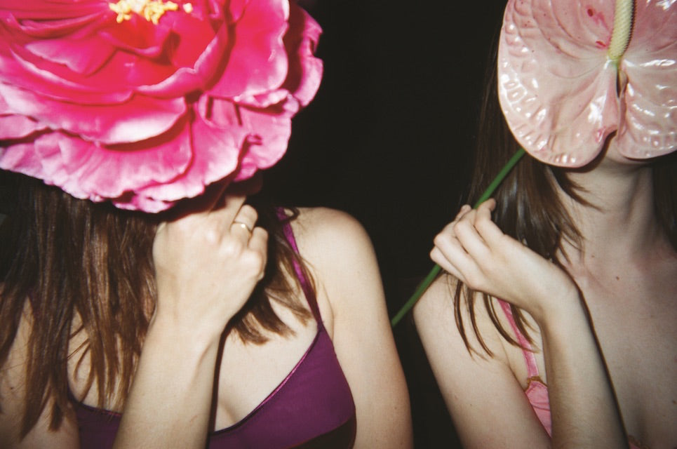 Women in bras holding large glass flowers over their faces.