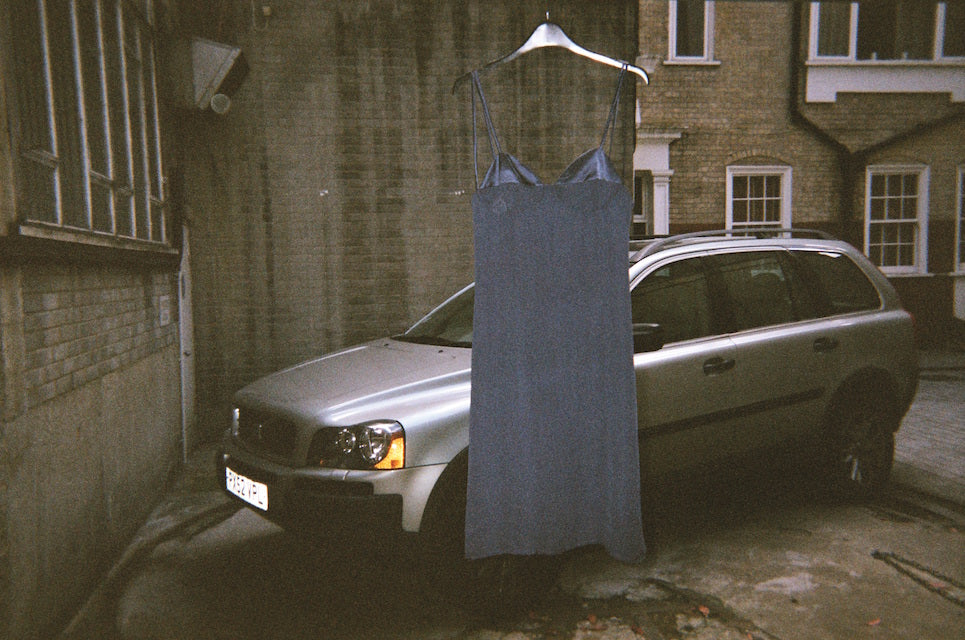 A blue chemise on a hanger in front of a silver car.