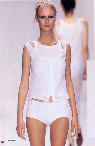 Woman in a white tank and white underwear walking on a runway.