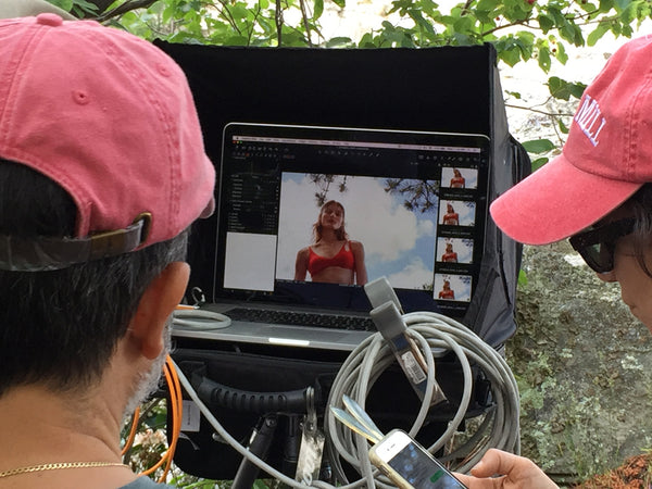 Two photographers in hats editing a photo of a woman in a red bikini top.