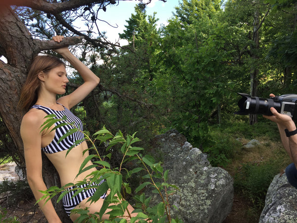 Woman in a black and white striped bikini holding onto a tree branch.