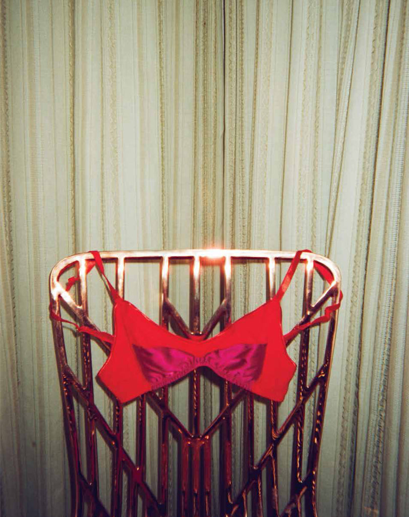Red bra hung on a gold chair with a white curtain in the background.